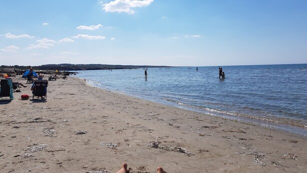 Una spiaggia con persone che camminano e siedono sulla sabbia, e il mare sullo sfondo.