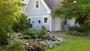 Una casa con un giardino che include uno stagno, circondata da vegetazione e un muro in pietra.