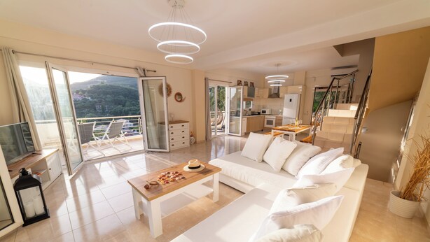 A modern living room with a white sofa, a wooden coffee table, and a balcony with a view of the hills. - Villa Parga – with private pool and authentic Sunset Panorama view! (parga)