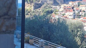 A balcony with a stone wall, potted plants, and a view of a hillside town with buildings and a castle-like structure. - Villa Parga – with private pool and authentic Sunset Panorama view! (parga)