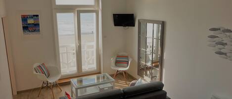 A living room with a sofa, a glass coffee table, a striped chair, a TV, and a large window with a view.