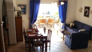 A dining area with a table and chairs, a sofa, and a view through curtains to an outdoor seating area. - Private Villa with superb seaview, swimming pool, garden, parking, pet friendly (Corfu)