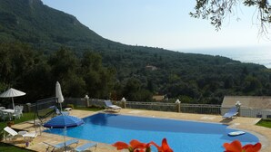 A swimming pool with lounge chairs and umbrellas, surrounded by a garden and a view of a mountainous landscape. - Private Villa with superb seaview, swimming pool, garden, parking, pet friendly (Corfu)