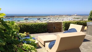 Terraza de madera con sillones de descanso y vista a barcos en una bahía.