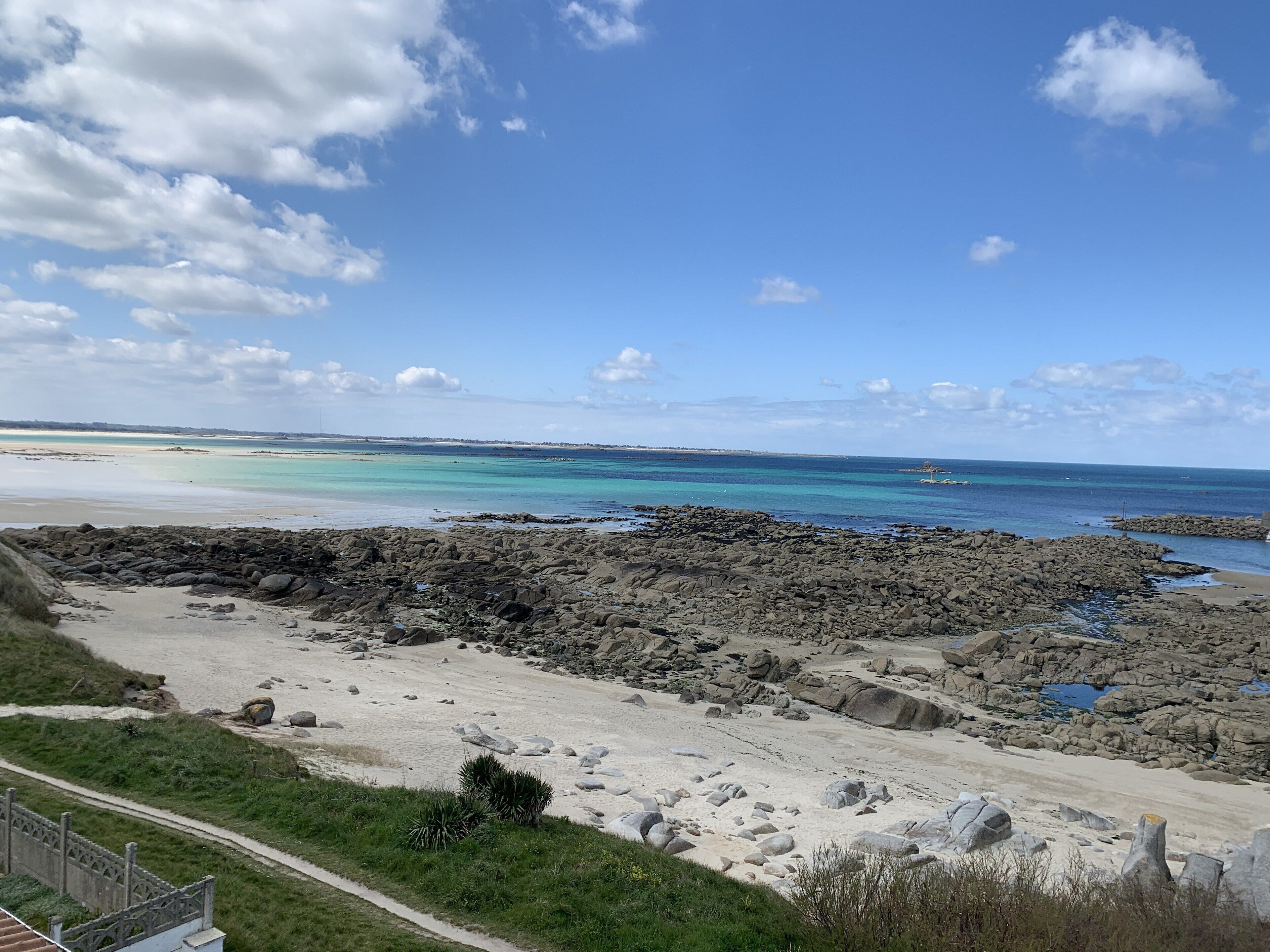 A coastal landscape with a rocky beach, a clear sky, and a distant shoreline.