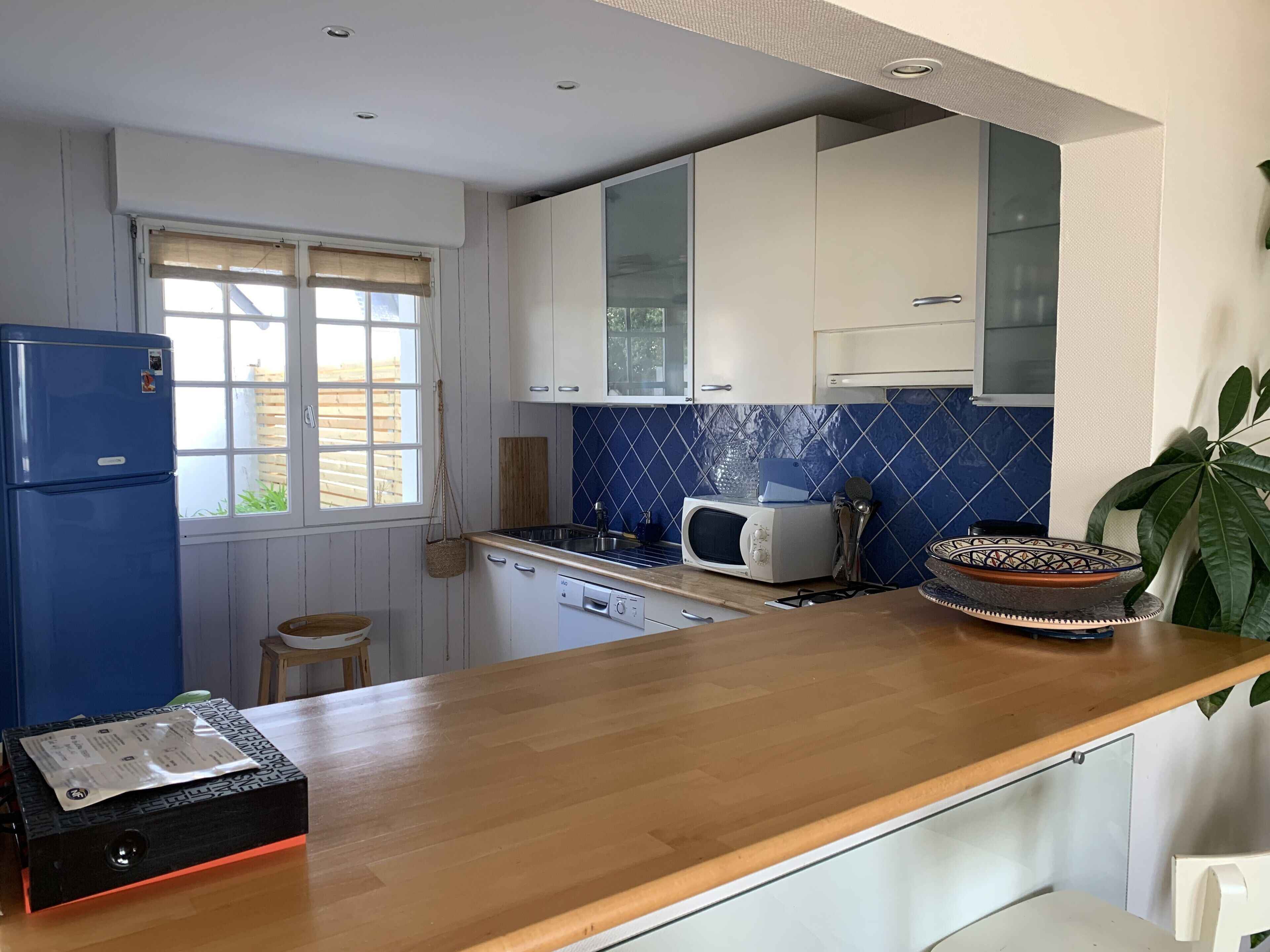 Een kleine keuken met witte kasten, een blauwe tegelachtergrond, een magnetron en een houten aanrecht.
