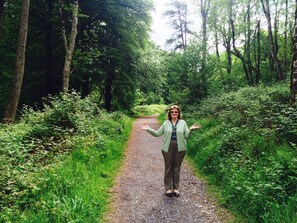 A woman standing on a gravel path surrounded by dense greenery and trees.