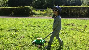 A child walking in a grassy field with a lawnmower.