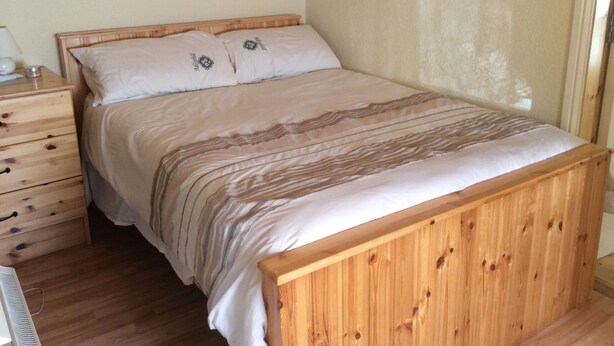 A wooden bed with a striped bedspread in a room with wooden walls and a wooden nightstand with drawers.