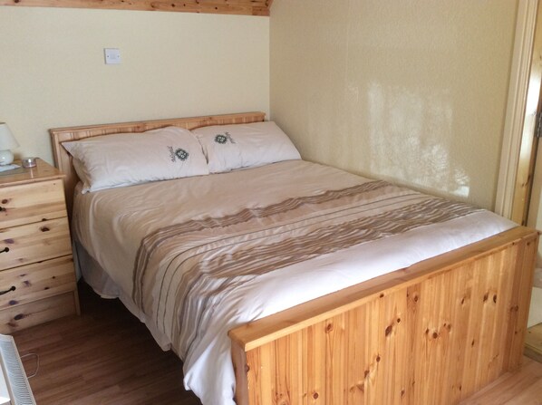 A wooden bed with a striped bedspread in a room with wooden walls and a wooden nightstand with drawers.