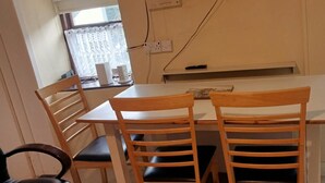 A dining area with a table and four chairs, a window with curtains, and a door with a curtain.