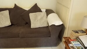 Un canapé marron avec deux coussins blancs et un plaid blanc.
