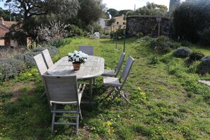 Een terras met een ronde tafel en vier stoelen, omringd door weelderige begroeiing en een stenen muur.