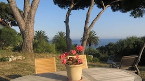A round wooden table with two chairs, a potted plant with red flowers, and a view of the sea. - Apartment/ flat - Hyères (Hyères)