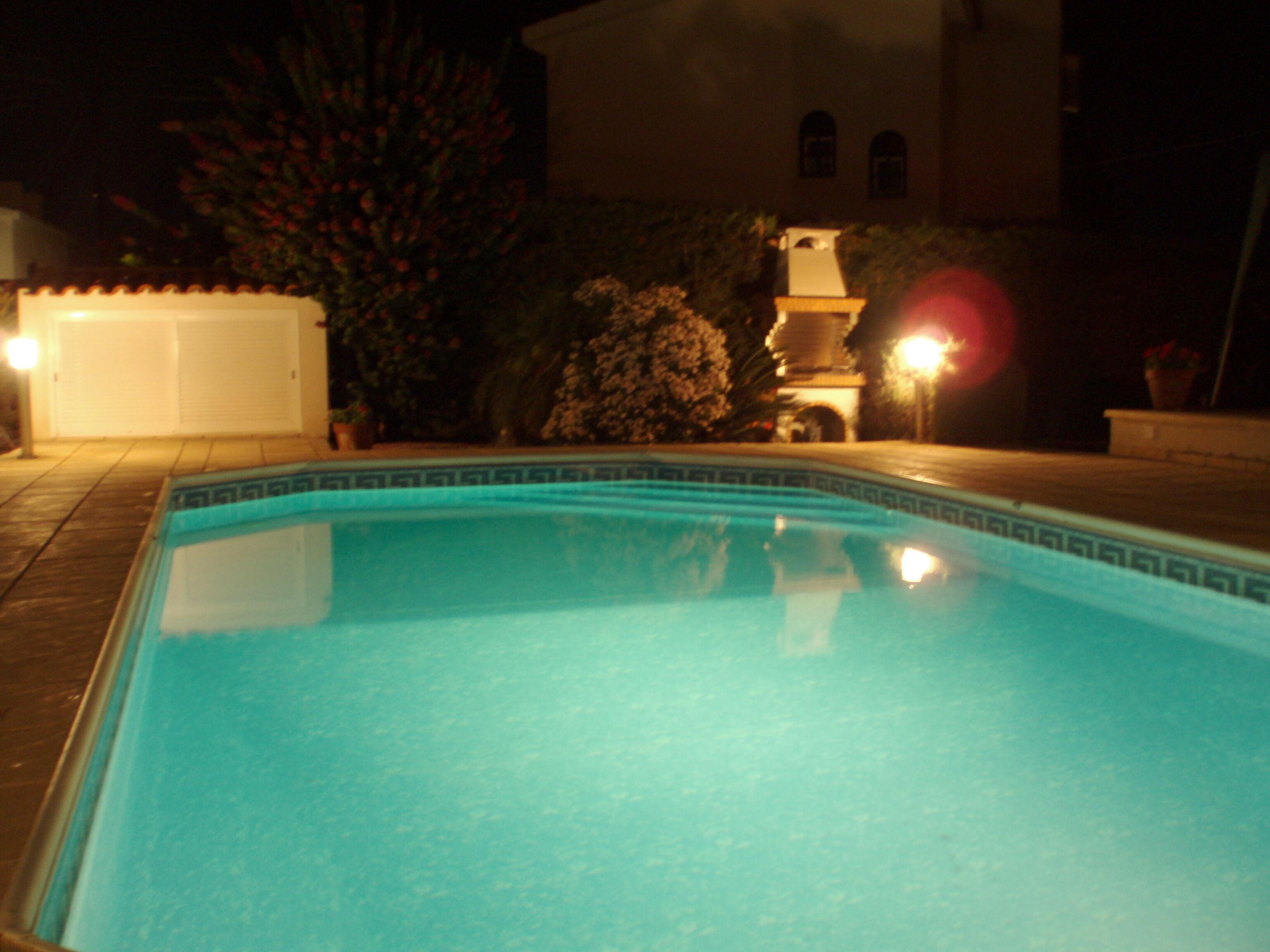 A swimming pool with a tiled edge, surrounded by a patio area with a lamp post and a potted plant.