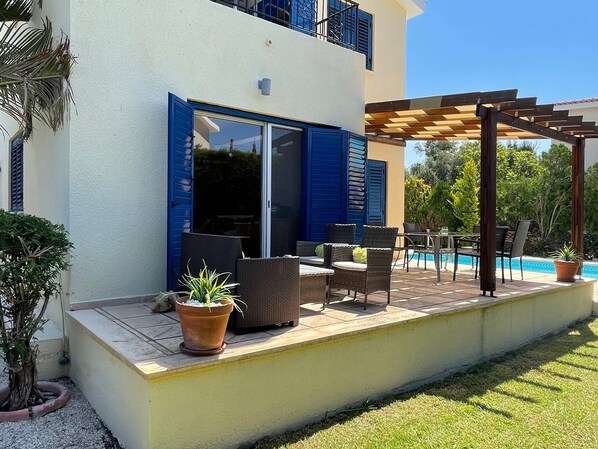 A covered outdoor patio with wicker furniture, a pool, and a pergola.