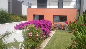 Un bâtiment moderne doté d’un toit plat, d’un petit jardin agrémenté de fleurs violettes et surplombant un ciel dégagé.