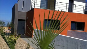 Un bâtiment moderne à deux étages, doté d’un toit plat, de grandes fenêtres et d’une façade dont les murs sont peints en blanc et en orange.