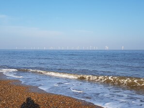 A beach with pebbles and waves, and wind turbines in the distance.
