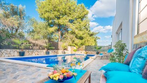 A poolside area with a stone floor, a wooden table with a fruit bowl, and a blue cushioned sofa. - Fabulous family Villa with pool, 500 m from the beach, for 6 people (Alcúdia)