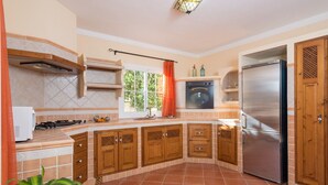 A kitchen with a stainless steel refrigerator, wooden cabinets, a built-in oven, and a window with curtains.