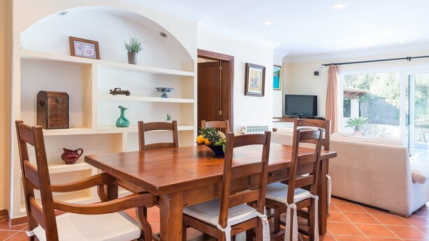 A dining area with a wooden table and chairs, a TV, and a view of the outdoors.