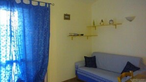 A living room with a sofa, a blue curtain, and wall-mounted shelves with decorative items.