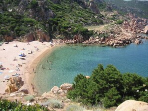 A coastal beach with clear waters, rocky terrain, and greenery. - Two-room apartment in stupendous Residence Sa Ventana (Badesi)