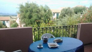 A round table with a blue tablecloth, two white chairs, a small white table lamp, a jar, and some papers on a balcony with a metal railing.