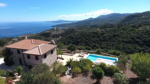 Une villa en pierre dotée d’une piscine, entourée d’une végétation luxuriante et offrant une vue sur un paysage côtier.