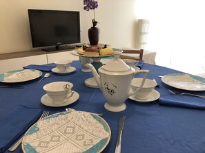 Une table à manger dressée avec des assiettes blanches et bleues à motifs, une théière, des tasses et un vase rempli de fleurs.