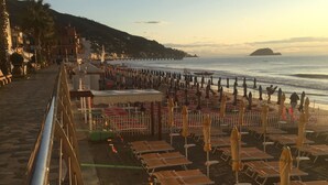 Une promenade en bord de mer bordée de rangées de chaises longues et de parasols, un chemin piétonnier et une vue sur la mer et les collines lointaines.