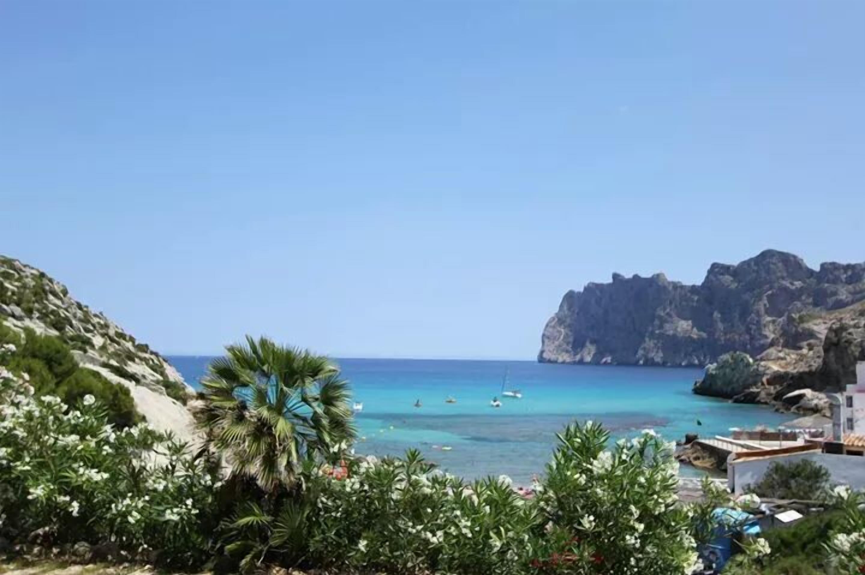A coastal view with rocky cliffs, clear blue sea, and boats.