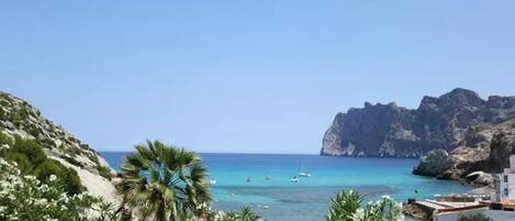 A coastal view with rocky cliffs, clear blue sea, and boats.