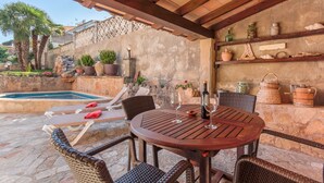 An outdoor patio with a pool, wicker furniture, and stone walls.