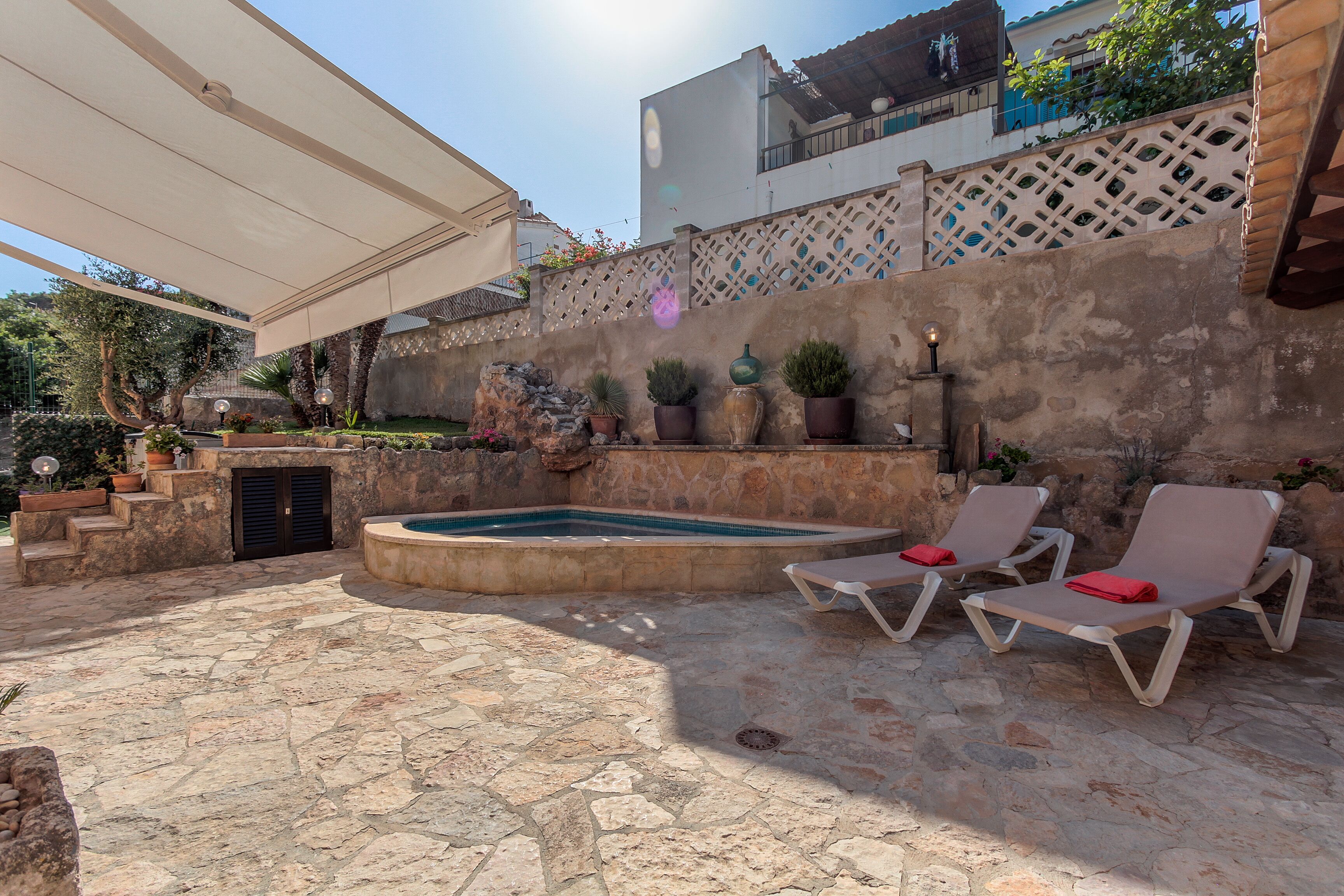 A stone patio with a hot tub, lounge chairs, and potted plants.