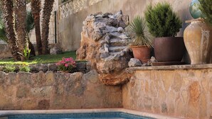 A pool area with a stone wall, potted plants, and a tiled edge.
