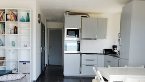 Moderni keittiö, jossa on valkoiset kaapit, ruokapöytä tuoleineen sekä kirjahylly, joka on täynnä kirjoja ja koriste-esineitä.