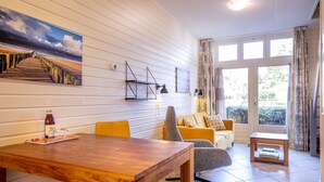 A living room with a wooden dining table, yellow chairs, a sofa, and a window with curtains.