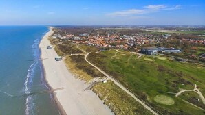 An aerial view of a coastal town with a beach, residential areas, and a golf course.