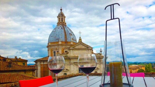 A table with two wine glasses and a bottle, set against a backdrop of a historic building with a dome. - Period residence located in the heart of Siena (Siena)
