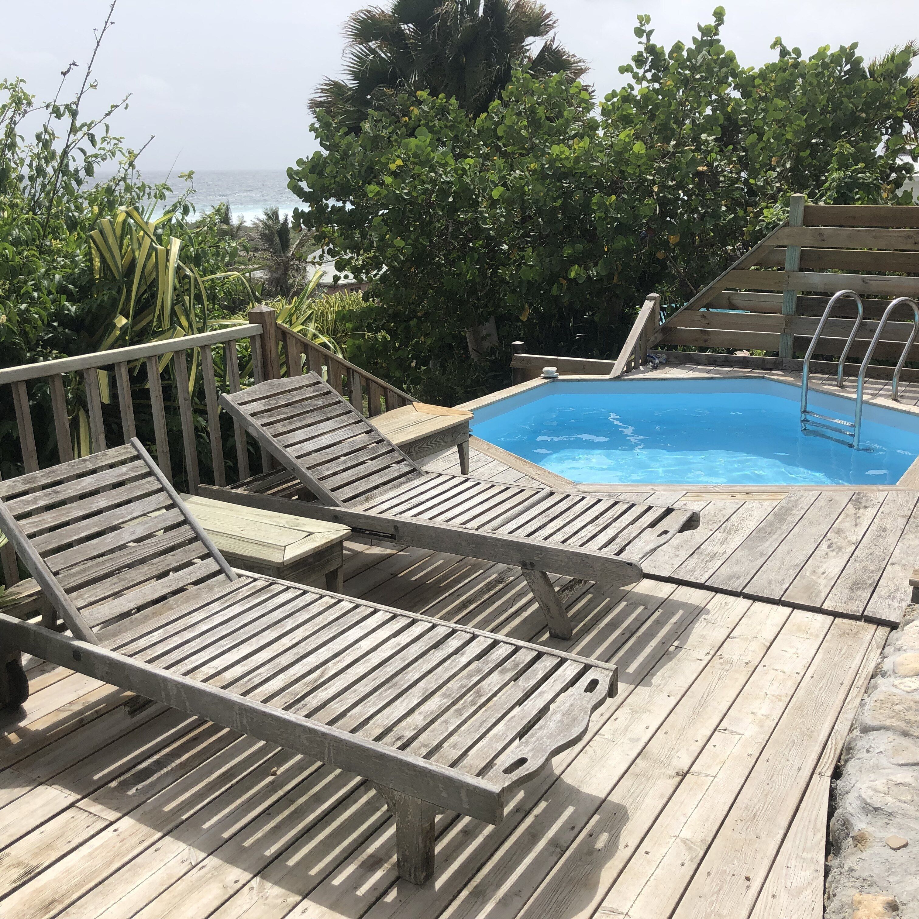 A wooden deck with lounge chairs and a pool.