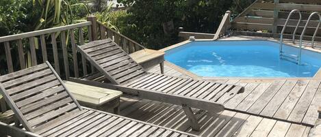 A wooden deck with lounge chairs and a pool.