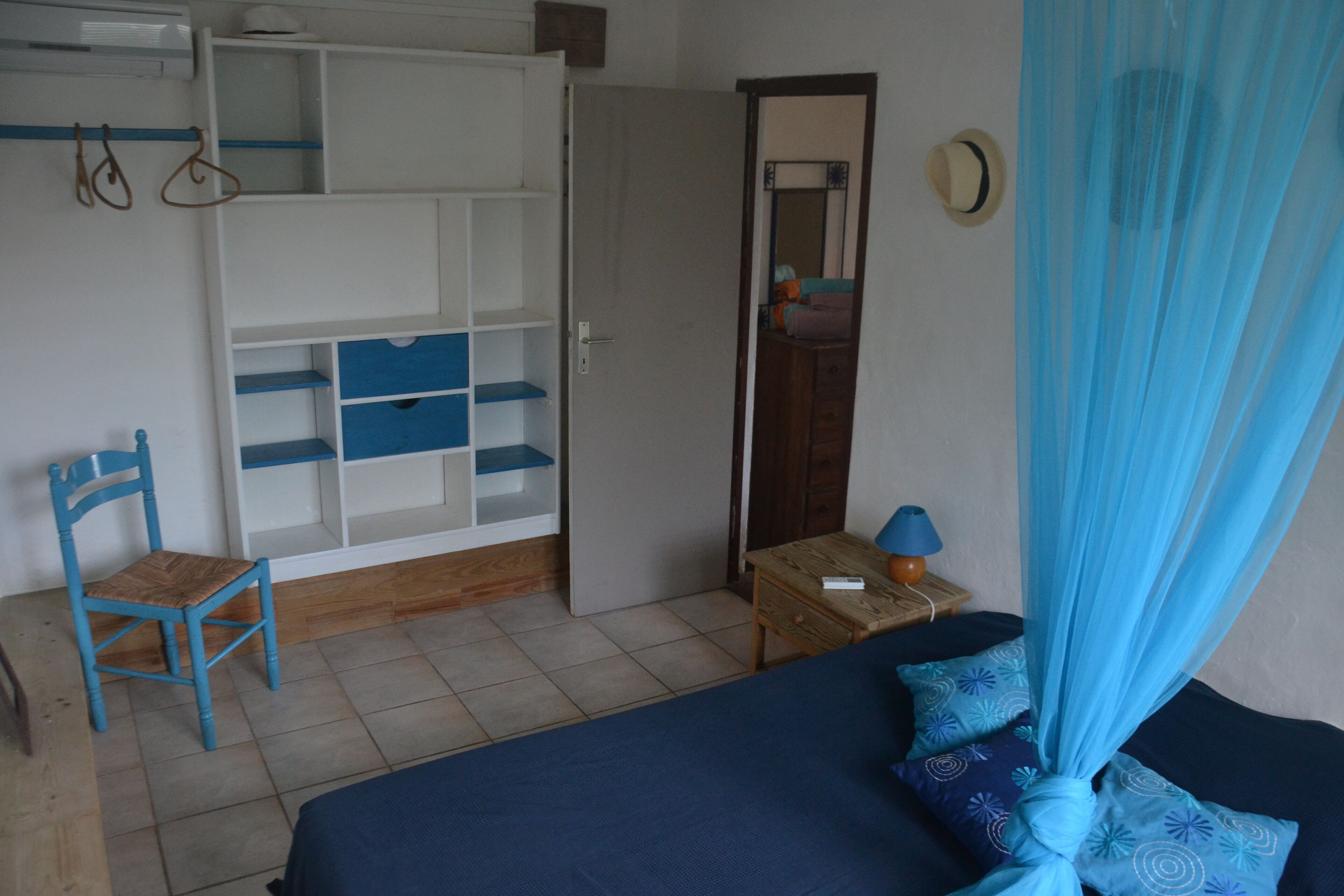 A bedroom with a bed, a wardrobe, a chair, a bedside table with a lamp, and a mirror.