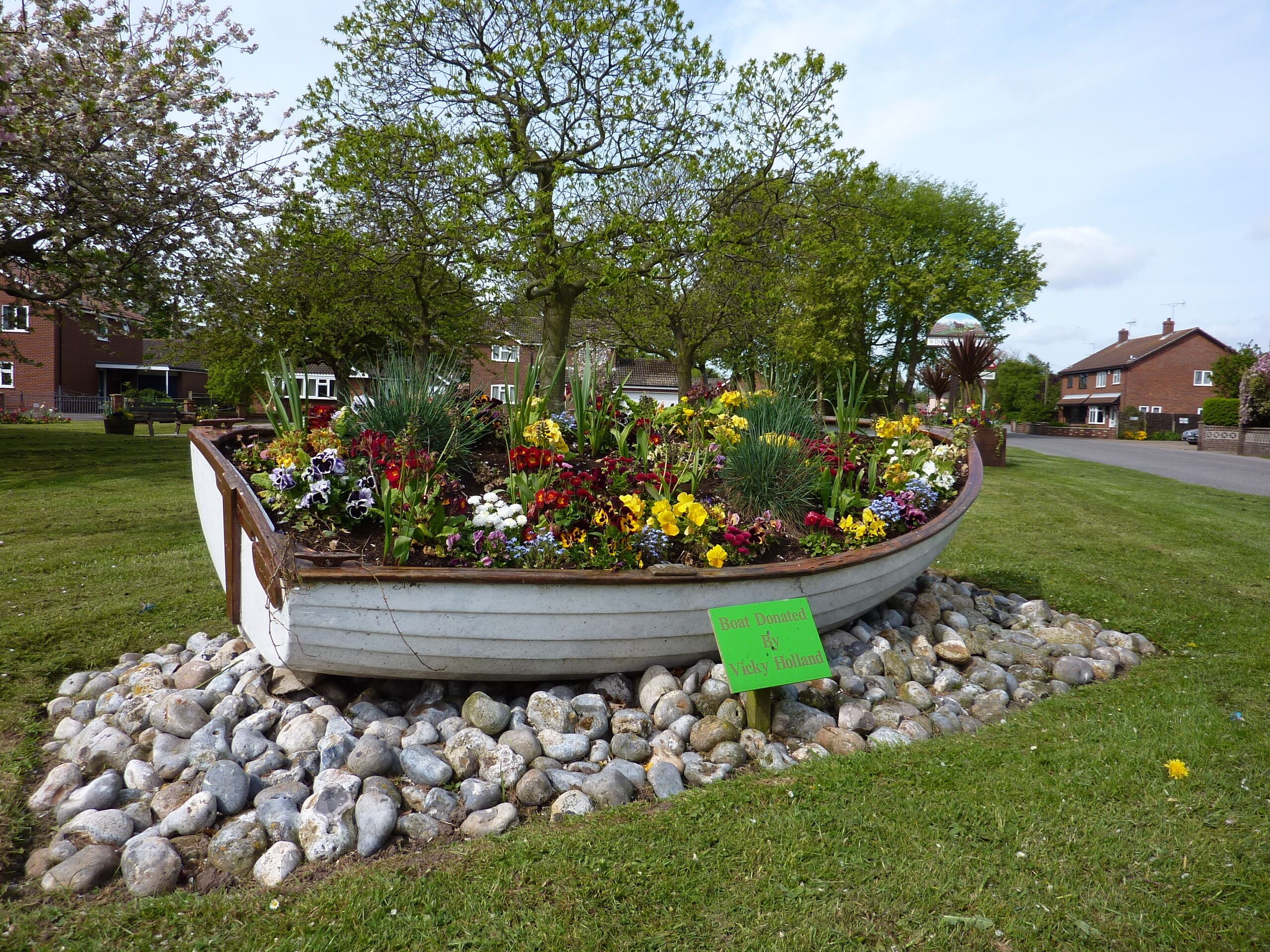 A flower bed in the shape of a boat with a sign stating it was donated by Vicky Holland.
