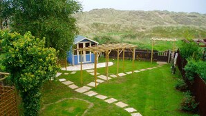 Ein Garten mit Spielbereich, einer Holzpergola und einem kleinen blauen Gartenhaus.