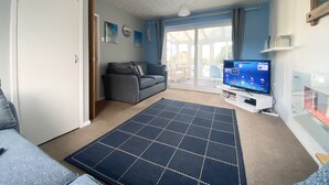 Ein Wohnzimmer mit einer Couch, einem Fernseher und einer Schiebetür zu einem Außenbereich.