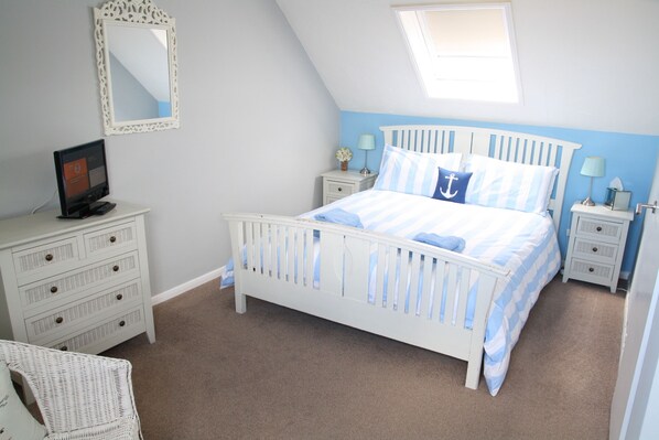 A bedroom with a white bed, a dresser, a chair, a nightstand, a lamp, and a mirror.