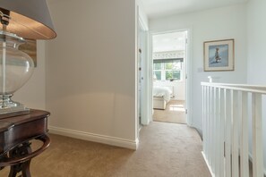 A hallway with a lamp, a framed picture on the wall, and a view into a bedroom with a window. - Driftwood Cottage, Brancaster, Norfolk (King's Lynn)