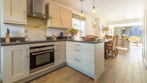 A modern kitchen with white cabinets, a built-in oven, and a large island with a sink. - Driftwood Cottage, Brancaster, Norfolk (King's Lynn)